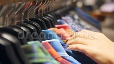 女人的双手用五颜六色的<strong>男装</strong>衬衫在衣架上奔跑。 年轻女孩在服装店为男友寻找礼物